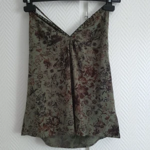 Top - En mörk grön top med blommönster som har en split i fram. Knyten i nacken och har en låg rygg, kontakta om intresserad💞