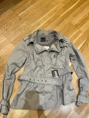 Cool trenchcoatjacka  - Cool trenchcoatjacka från Kjulo. Massa coola detaljer som skärp mm. Mer som en M i storlek. Gråbeige i färgen
