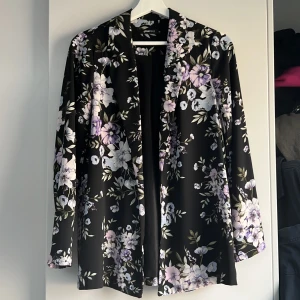 Mönstrad kavaj - Svart kavaj med lila och vita blommor, inga defekter. Jättefin men kommer aldrig till användning 