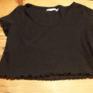 En svart lite kortare t-shirt med lite mönster på ärmarna och vid slutet av tröjan den e även uringad fram. Från Lager 157.