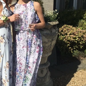 Klänning - Maxiklänning/långklänning. Mönstrad(blommig) klänning 😍 Hög ringning, armlös med fina volanger. Stretch i midjan med fin knäppning back.    Använd vid ett tillfälle (bröllop). 