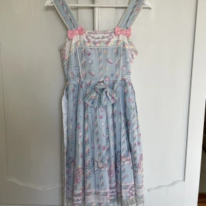 FAKE Angelic Pretty klänning - OBS FAKE Angelic Pretty ”Sugary Carnival” klänning med matchande rosett. Använt begagnat skick men fin ändå