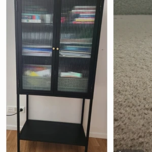 Nicke Vitrinskåp Mio  - Köptesför några månader sen från Mio.Helt ny som oanvänds och jättefina.Den har ett mycket tätt utseende i rummet. Säljs pga. Flyttning.Nu kostar i butik 2000kr som jag köpte också. svartpulverlackerad metall, 2 glashyllplanoch dörrar,dekorglas och 1hylla