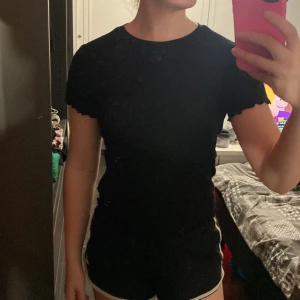 Svart t shirt - En vanlig svart t shirt med volanger på ärmen och slutet av tröjan! Materialet är också ribbat