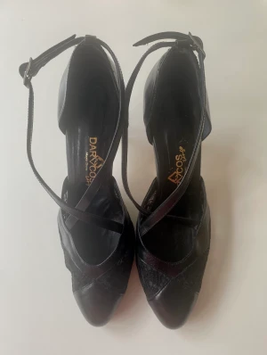 Svarta tango-/dansskor i strlk 39 - Svarta tangoskor i skinn och spets med fin rem som går i kors över foten. Märke Darcos, inköpta i Buenos Aires. Använda ett fåtal gånger. Storlek 39.