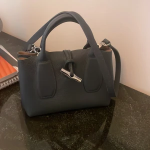 Longchamp väska - Säljer denna unika Longchamp väska i blå/grå färg köpt i butik i Frankrike! Äkta!  Helt oanvänd och inga skador! Är öppen för förslag på  pris!