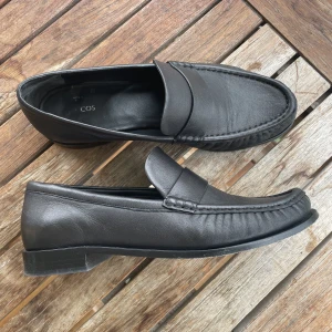 Loafers i skinn storlek 39 - Loafers i skinn i strl 39. Köpta på COS. De är lite smalare och mjukare än vanliga loafers som annars lätt glappar. Använda ca 5 gånger så de är i nyskick!  Nypris 1250kr