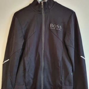 Hugo boss hoodie - Hoodie i svart, grå (reglekterande) detaljer. Dragkedja. Finns tillhörande byxor. Fint skick.