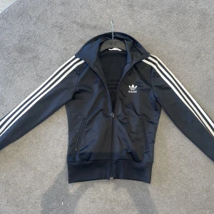 Svart Adidas Zip Tröja - Fin svart adidas zip tröja i storlek xs dam men passar superbra för killar bara att den är mindre än en man tröja i xs. Bra skick 9/10. Dyker det upp frågor är det bara att fråga 😊
