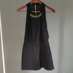 Byxdress  - Kort byxdress som är snygg med partykänsla. Uppdelad i två olika material (se bild tre) överdelen är i ett transparent och lätt tyg som är lite lager på lager, med en öppen rygg, knäpps med två knappar i nacken. Fickor och ett påsytt halsband. 