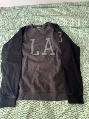 Tröja med LA tryck  - Jag säljer nu min tröja för att den är för liten. Den är i riktigt bra skick då den knappt har använts. Passar för någon som normalt använder L eller M.