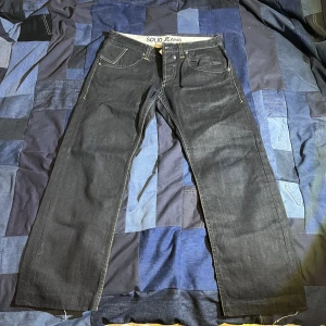 Solid jeans - Detaljrika jeans, midja 32, innerlår 28/68cm, totallängd 94 cm, benöppningens längd 20,5cm.  Saknar tyvärr knappen på högra bakficka:/ annars otorligt snygga jeans. Dm vid frågor