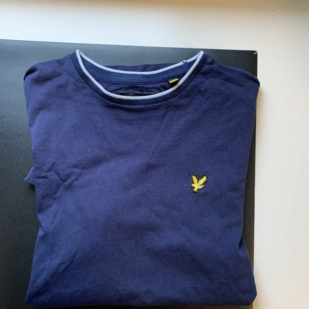 En mörkblå Lyle & Scott t-shirt i storlek S.  Mönster på både kragen och ärmarna där passformen är normal. T-shirts.