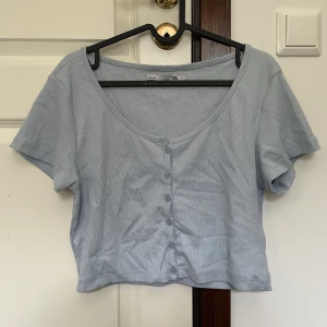 Cropped tshirt - Söt ljusblå kort tshirt med knappar i fram. Använt kanske en gång, sen aldrig mer så någon annan kan få användning av den.