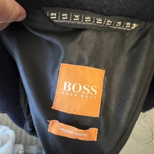 Hugo Boss Jacka - En super snygg blå jacka/kort kappa från HUGO BOSS. I stort sätt oanvänd och har endast hängt. Nypris: 4000kr.  Herr(storlek): UK50. Han på bilden har vanligtvis en M/L i kläder och jackor.