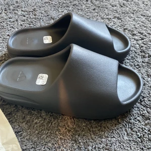Adidas yeeze slides onyx  - Jag säljer mina yeeze slides onyx som jag köpte på adidas CONFIRMED APP. Helt nya. Box och kvitto följer med. Skriv om du har några funderingar