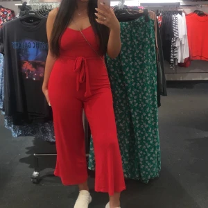 Röd jumpsuit/byxdress i strl 34 - Röd ribbad jumpsuit/byxdress med avtagbar knytning i strl 34. Stretchigt material som även passar 36-38. Använd flertal ggr. Jag är 158 cm.