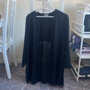 Tunn cardigan - En tunn, svart, lång cardigan. Lite öppen nertill mot sidan av låren, sömmen har släppt lite och gjort ”hålen” högre men ingenting som direkt syns. Går att sy igen om man så vill. 