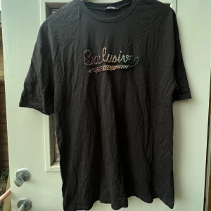T-shirt från Zara - Mörkgrå t-shirt från zara med texten ”exklusive” på skriven i färgglada pärlor.