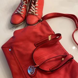 Väska och skor  - Skorna är använda några gånger, skosnörena är lite smutsiga. Väskan är nästan aldrig använd och i bra skick. Färgen är rödrosa aktig. Skorna är storlek 40