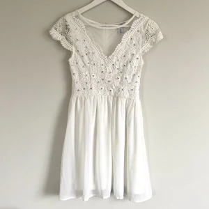 Studentklänning Nelly  - En oanvänd vit klänning från Nelly. Den har fina strassdetaljer över bröstet och fint spetstyg vid ärmarna. Passar perfekt till student eller skolavslutning!  Storlek: 34 Material: 100% polyester Skick: Oanvänd