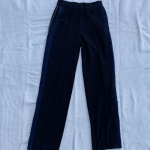 Monki trackpants - Trackpants från Monki i svart med en mörkblå och vit rand på sidorna. Tyvärr för små för mig men jättesnygga! Har en dragkedja längst ner på benen som man kan dra upp om man vill, se bild 2. Raka i benen.