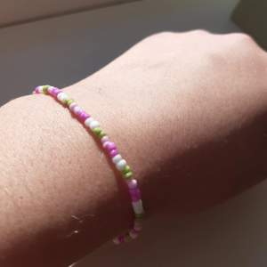 Ett armband med små rosa, vita och gröna pärlor. Tips var försiktig det KAN kanske gå sönder!🤗