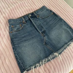 Jeanskjol från Levi’s i storlek W25. - Jeanskjol som är köpt på Levi’s. Storleken är W25. Har lite fransar ner till. Kjolens längd är 37 cm.  
