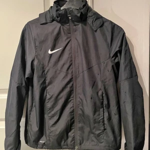 jacka - Vind & vattenresistent svart lättviktsjacka. Dragsko insytt i fåll nertill till att reglera om man vill. Avtagbar huva.  Strl 148-158c passar mig med xs 💕