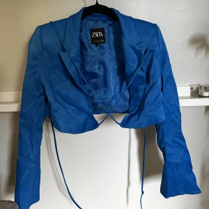 Blå Cropped kavaj - Snygg blå satin kavaj från zara. Den är Cropped och går och knyta på några olika sett med snören! Köpt här på Plick men jag har endast använd den en gång