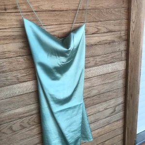 Kort grön sidenklönning - Jättefin kort klänning i sidenimitation. Har tyvärr ett hål och en fläck som inte går av och därför säljer jag för billigt pris