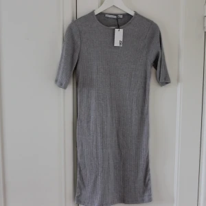 Ribbad klänning  - Oanvänd ribbad grå klänning som går en bit ovanför knäna i ett strechigt material. 🤍 Köparen står för frakt. Hör av dig om fler bilder önskas eller om du har någon annan fråga. 