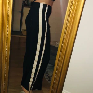  - Vida byxor i svart med ljusrosa streck på sidan. En liten slits längst ner i benslutet. Bara provade.