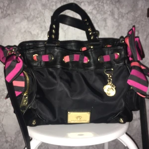  - Väskan är svart med guld detaljer och med ett rosa,svart,lila band som går runt väskan och väskan har 5 fack där du kan lägga dina saker 