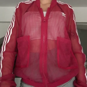 Adidas Track Jacket - Supersnygg Adidas track-jacket i mörkrosa! Genomskinlig och meshliknande material som du kan matcha med någon cool bh eller tröja under eller helt för sig själv ✨✨ DM vid intresse.