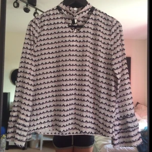  - En tunn blus mes choker detalj och volanger vid ärmslut.