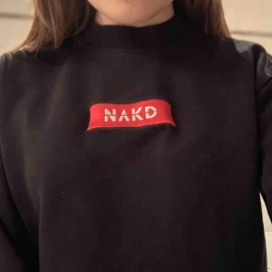  - Det här plagget är en svart vanlig sweatshirts med en text i mitten där det står na-s och den är då från na-kd och är i storlek xs och den är i en vanlig passform och jätte mysig och bekväm men också väldigt snygg 