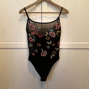 Body med brodyrdetaljer - Supersnygg halvt genomskinlig body från Zara med brodyrdetaljer. Helt oanvänd med prislappen kvar. Nypris 189 kr. Finns möjlighet att reglera banden på baksidan så storleken är anpassningsbar.  Kampanj: KÖP 3 BETALA FÖR 2