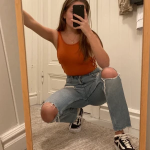 Orange Bodysuit i XS - Bodysuit i bra skick från BikBok som kan öppnas längst ner. Den är öppen på sidorna i ett rutigt mönster och ger en snygg siluette. Köparen står för frakten (vet ej hur mycket frakten kommer kosta, priset jag satt är en gissning) 