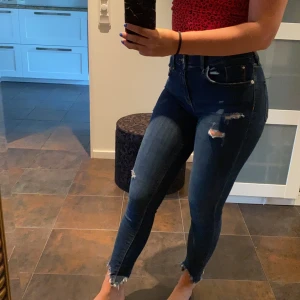 Jeans från River Island - Mörkblåa Jeans från River Island med slitningar. Mellanslag i midjan, går ungefär till naveln. Använda men inget fel på dem. Säljer pga att de är för små. Storlek 10, skulle säga att de passar 36 men de är stretchiga så även något större. 150kr +frakt