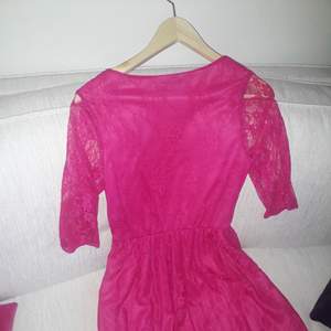 En rosa/röd klänning som sitter  snyggt.  Slutar strax innan knäna.  Fin spets som gör den extra lyxig.