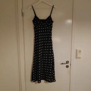 Prickig långklänning  - En prickiglångklänning som slutar vid vaderna. Dragkedja i sidan samt reglerbara axelband. 