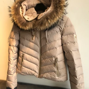 Hollies jacka  - Säljer min Hollies dun-jacka då den inte kommer till användning. Klassiska kort beigea modellen med kanin päls. Jag köpte denna förra vintern och använde den endast en säsong. Jackan är precis kemtvättad och inte använt den sedan dess. Jackan är i jätte bra skick nästan som ny. Alla guld detaljer är kvar och kanin pälsen på luvan är i perfekt skick. Nypris 3000kr mitt pris 1100. Pris kan diskuteras vid snabb affär. Kan mötas i Norrköping men kan också frakta. Köparen står för frakten. Strl 36. XS/S. Självklart är den äkta. 1100 kr