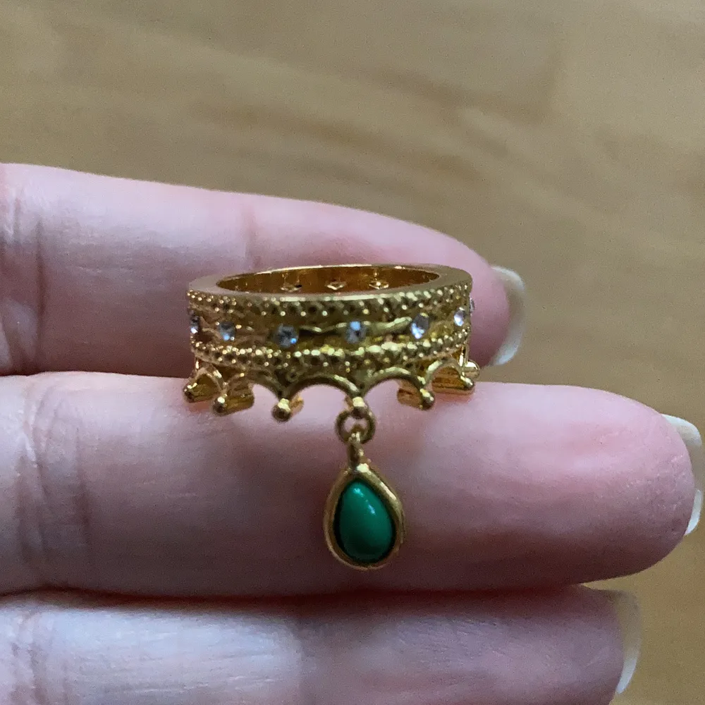 Otroligt söt helt ny ring i guldfärg ca 16,7 mm. Är formad som en krona med vita gnistrande stenar och en grön hängande pärla. . Accessoarer.