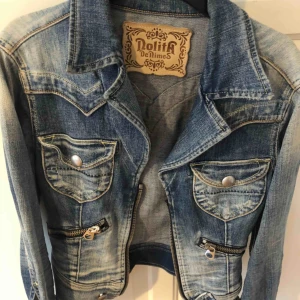  -  Nolita denim jacka, jeans blå jacka från Nolita med ett tryck av svag leopard på ryggen, framtill finns dragkedja och fickor plagget är inte använt många gånger men på den vänstra armen saknas en knapp. Inköpspris 700kr