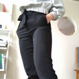  - Svarta kostymbyxor med knytbälte i midjan. Lösa i modellen med en liten slits längst ner. Frakt tillkommer!