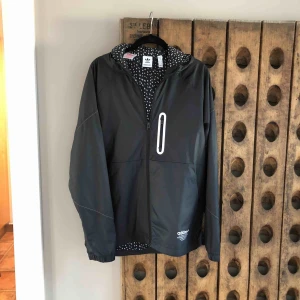  - Ny vindjacka från Adidas mönstrat foder,fickor,fast huva,bröstficka längd fram 68,längd bak 74,bröstvidd 106,armlängd 63