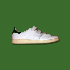 Adidas Stan Smith  - Adidas Stan Smith med kardborreband.                                    Storlek EU43 1/3 eller US9 1/2.                                                  Färg: Vit/Grön. Syns ej så bra på bild 1 men grön häl.              Skick: 6/10 allmän användning inga tydliga defekter.                KÖP NU 200kr eller kom med bud i DM! Frakt tillkommer (63kr).  