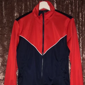 Kofta - En kofta i mörkblå och röd. Som har en krage som går upp vid halsen.