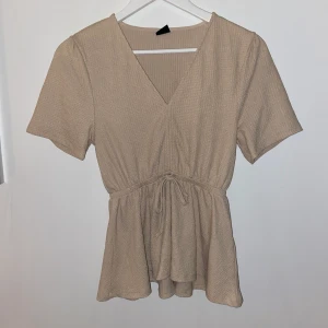 Beige blus strl S - Kortärmad topp från GinaTricot i strl S, knytning i midjan som ger en snygg figur. Frakt enligt postnord💛